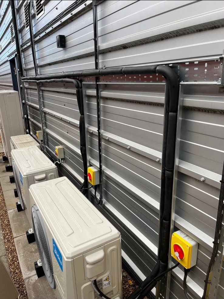 Commercial air conditioning outdoor units and refrigerant conduit installed along an industrial building wall