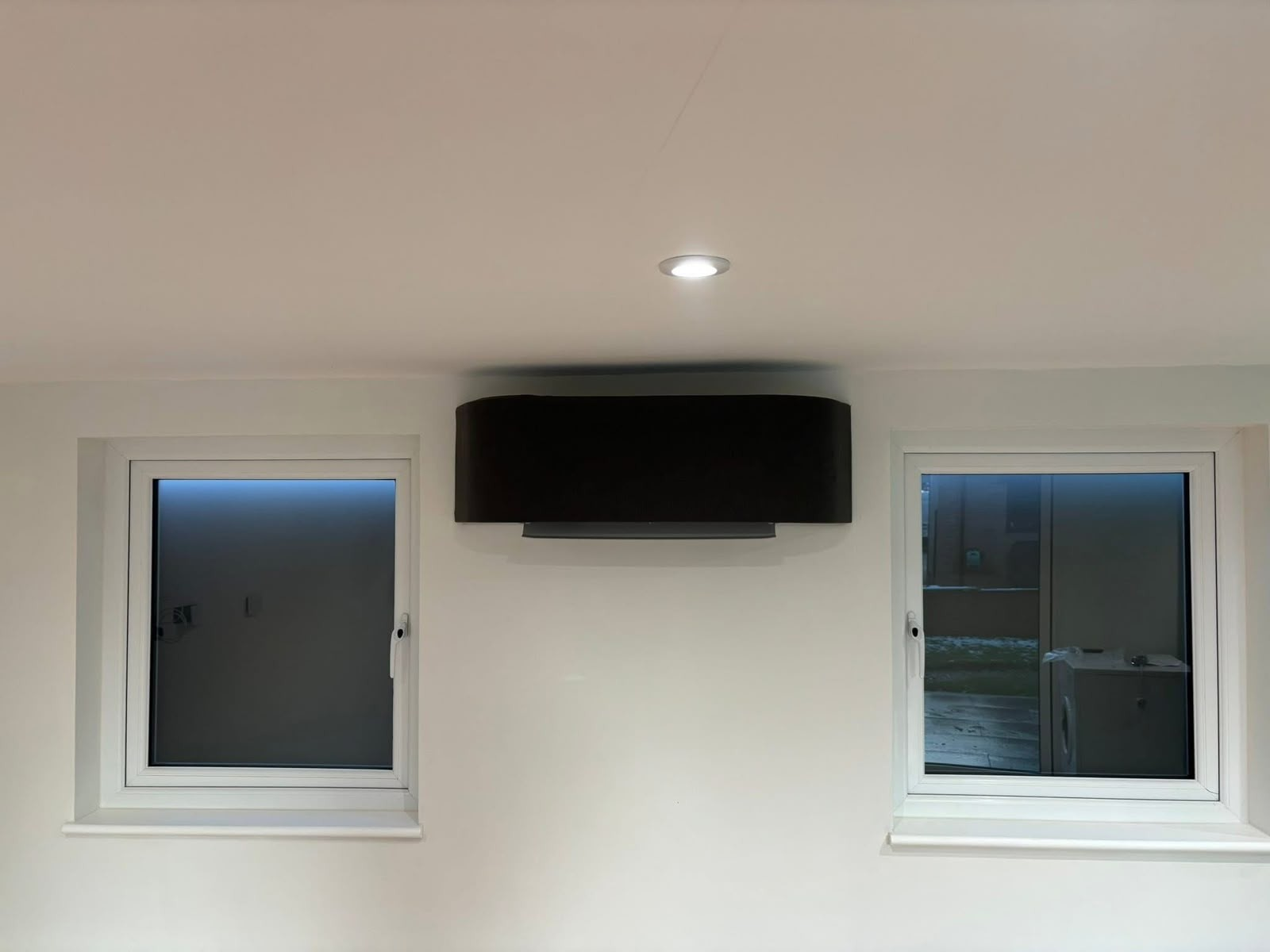 Black low-wall air conditioning unit installed between two windows in a home